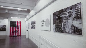 Wall of Josue's gallery show featuring American flag written over, childhood photo manipulated, I'm older than America painting.