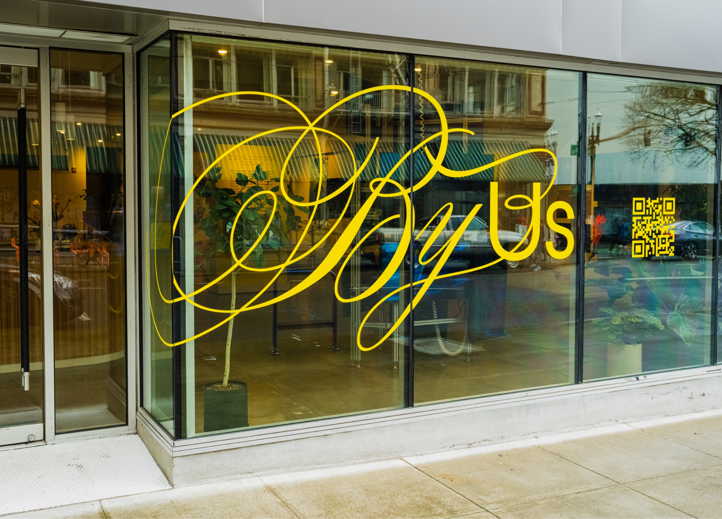Gallery front window with large vinyl letters reading By Us with QR code