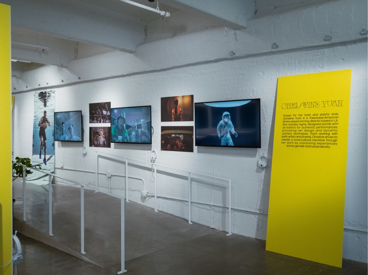 Wall of gallery showing a poster of Nike Zion then 6 TV's showing artist's work, Large yellow board with Christine Yuan's bio.