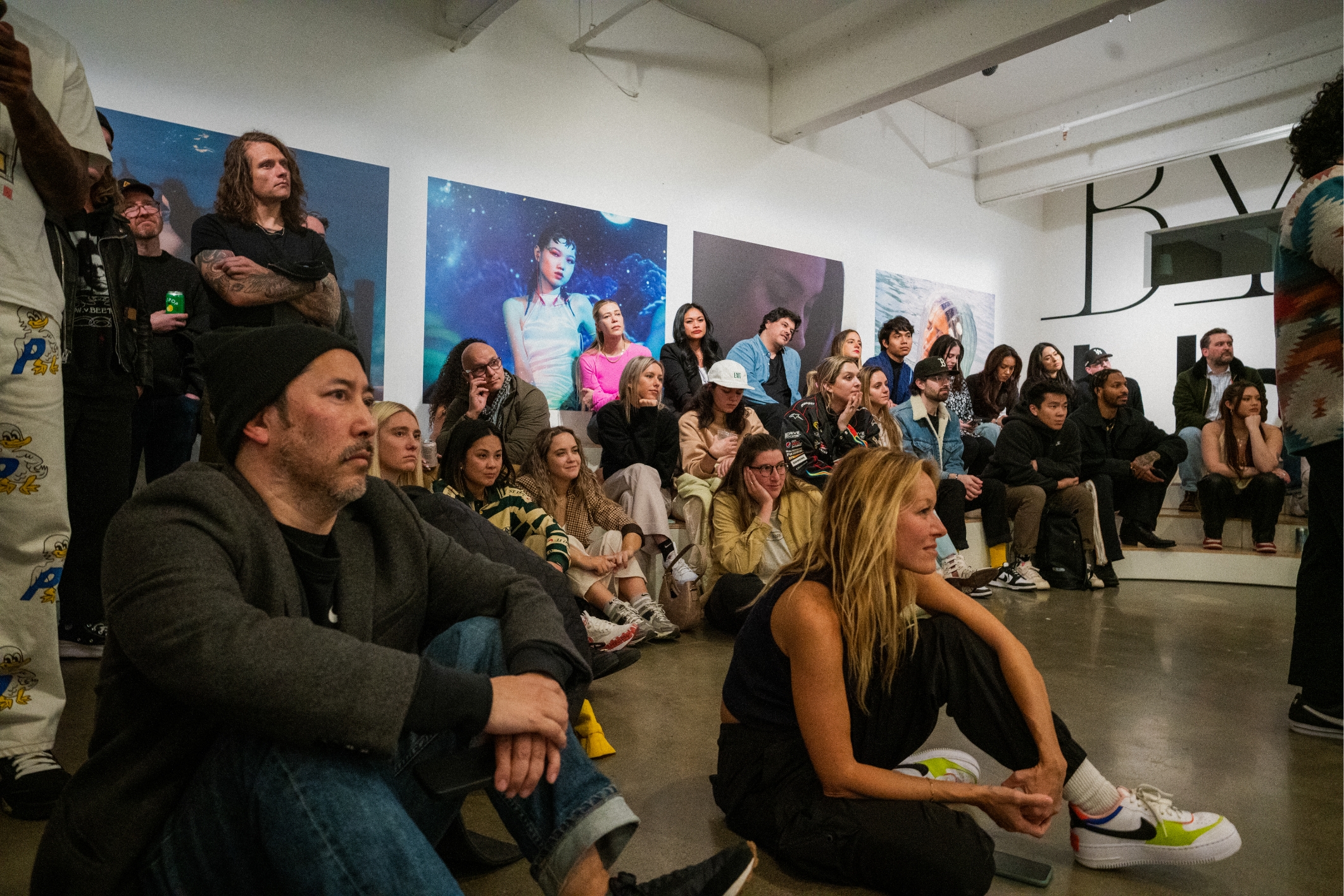 Large group of gallery attendees sitting listening to artists speak in gallery