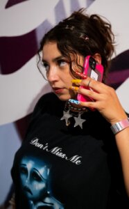 Woman with long colorful nails holds phone to ear posing in front of gallery wall