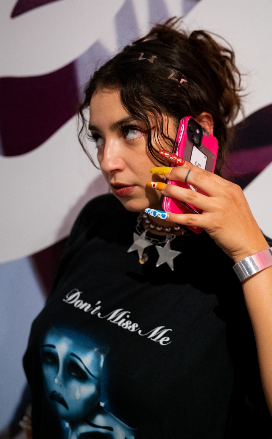 Woman with long colorful nails holds phone to ear posing in front of gallery wall