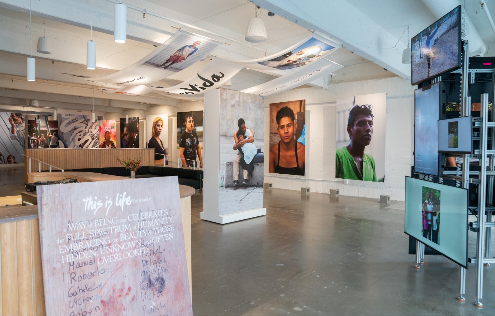 View of entire gallery and Esto es Vida show from the gallery entrance. Featured is greeting sign which reads: a way of being that celebrates the full spectrum of humanity, embracing the beauty of those hidden, unknown and often overlooked.