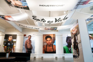 Art Gallery with fabric banners on ceiling reading INDUSTRY ONE, Esto es Vida and mexicana. Large portrait photos are hung on the wall