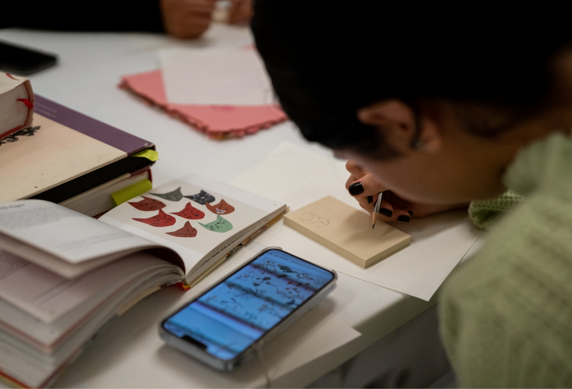 A woman is writing on a piece of paper with a cell phone.