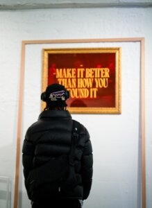 A man looking at a framed poster that says make it better than how you could.