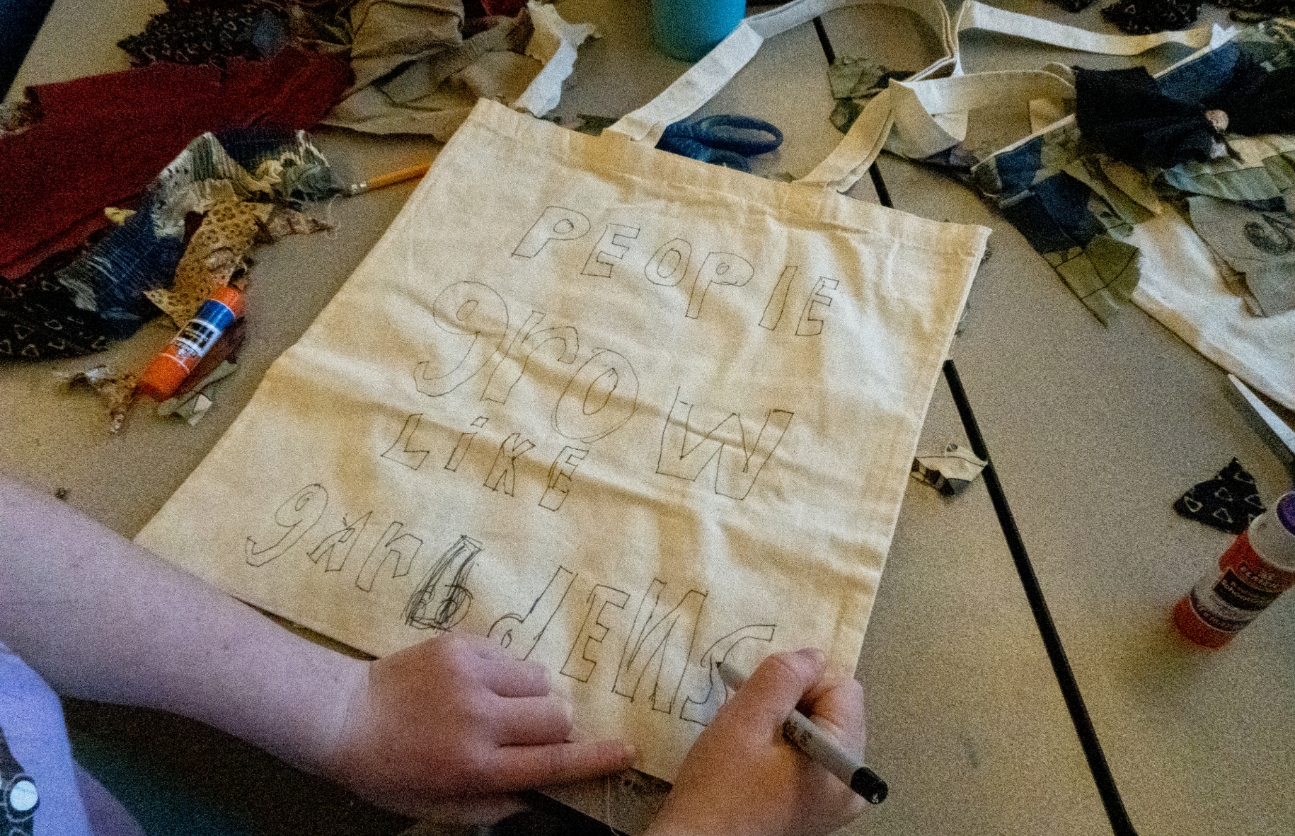 young person writes people grow like gardens on tote bag