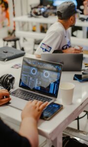 Person using a laptop with DJ software on the screen, sitting at a table with another person in a casual setting.
