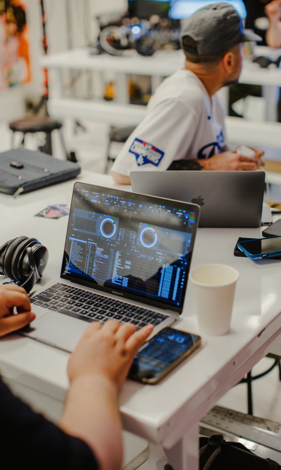 Person using a laptop with DJ software on the screen, sitting at a table with another person in a casual setting.