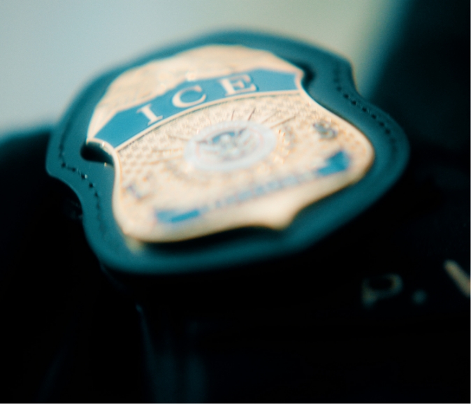 Close-up of a badge with the letters "ICE" on it, attached to a dark surface.