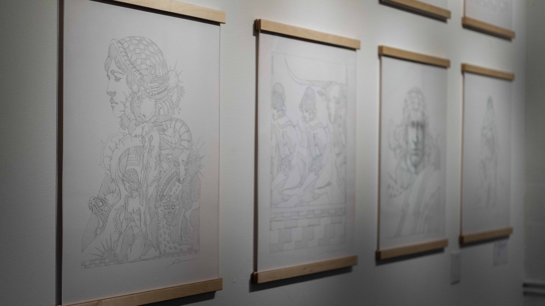 A series of framed pencil sketches hang on a gallery wall, each depicting different scenes and figures.