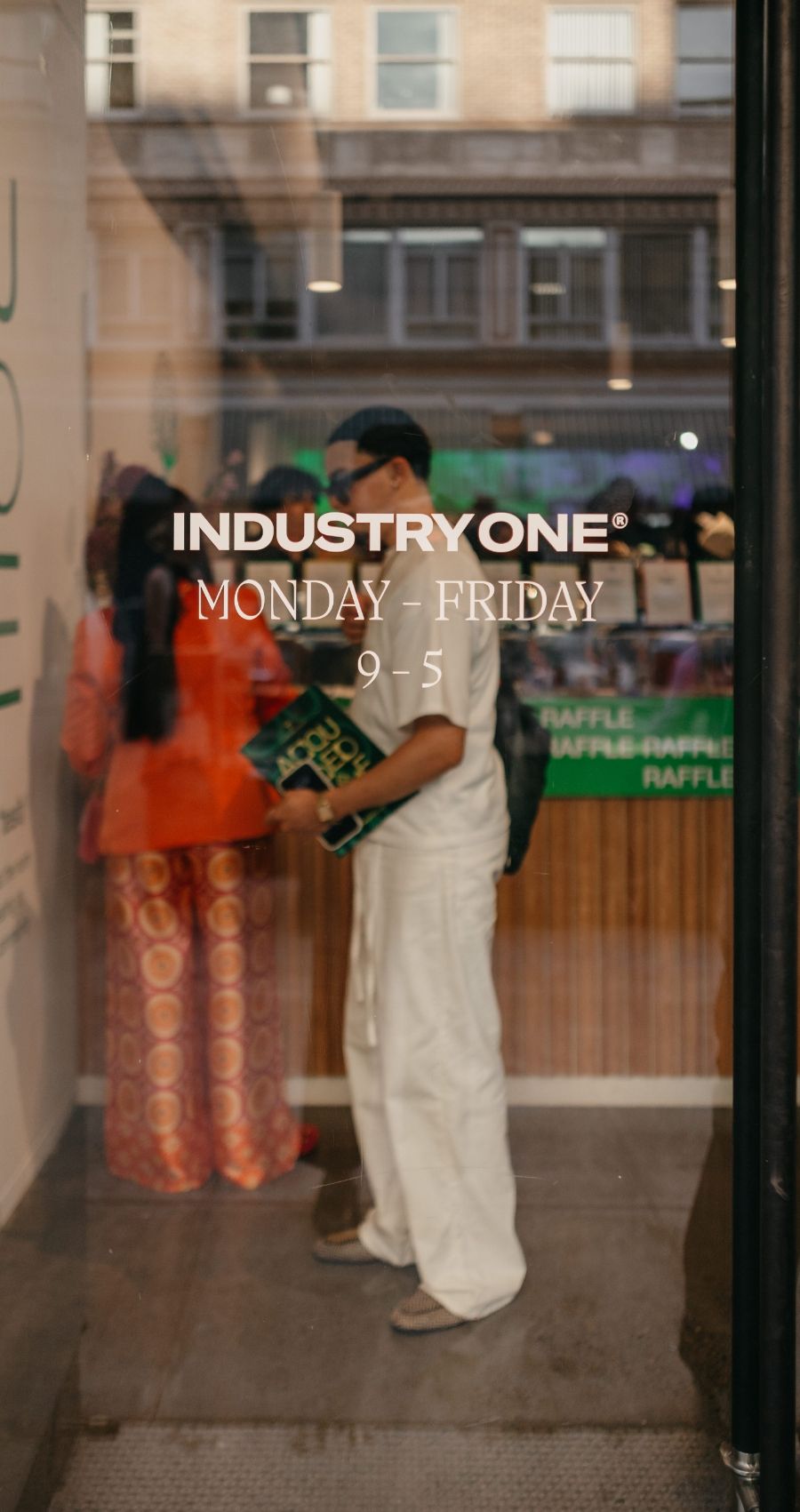 Individuals are seen standing inside a store. A glass door displaying "IndustryOne Monday - Friday 9-5" in white text is in the foreground.