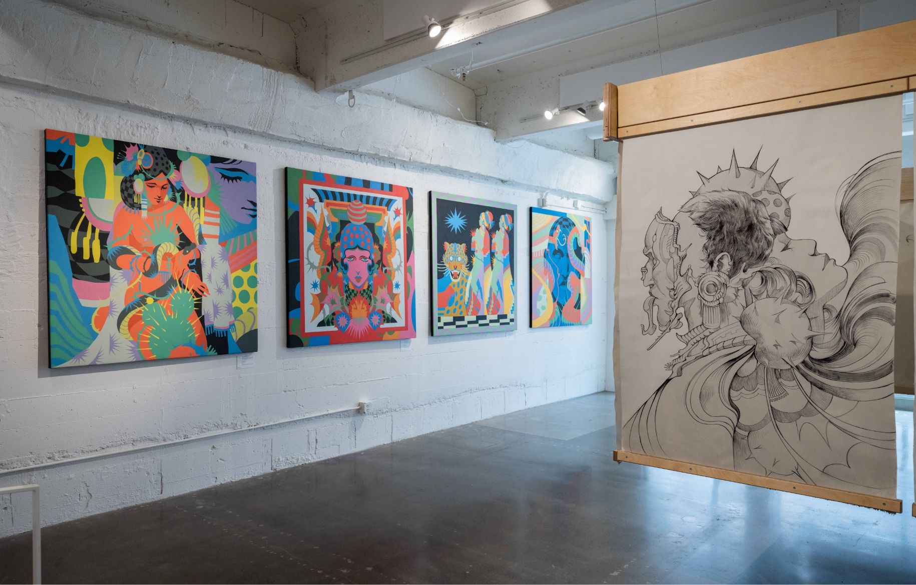 An art gallery displaying four colorful abstract paintings on a white wall and a large monochrome sketch hanging from a wooden frame in front.