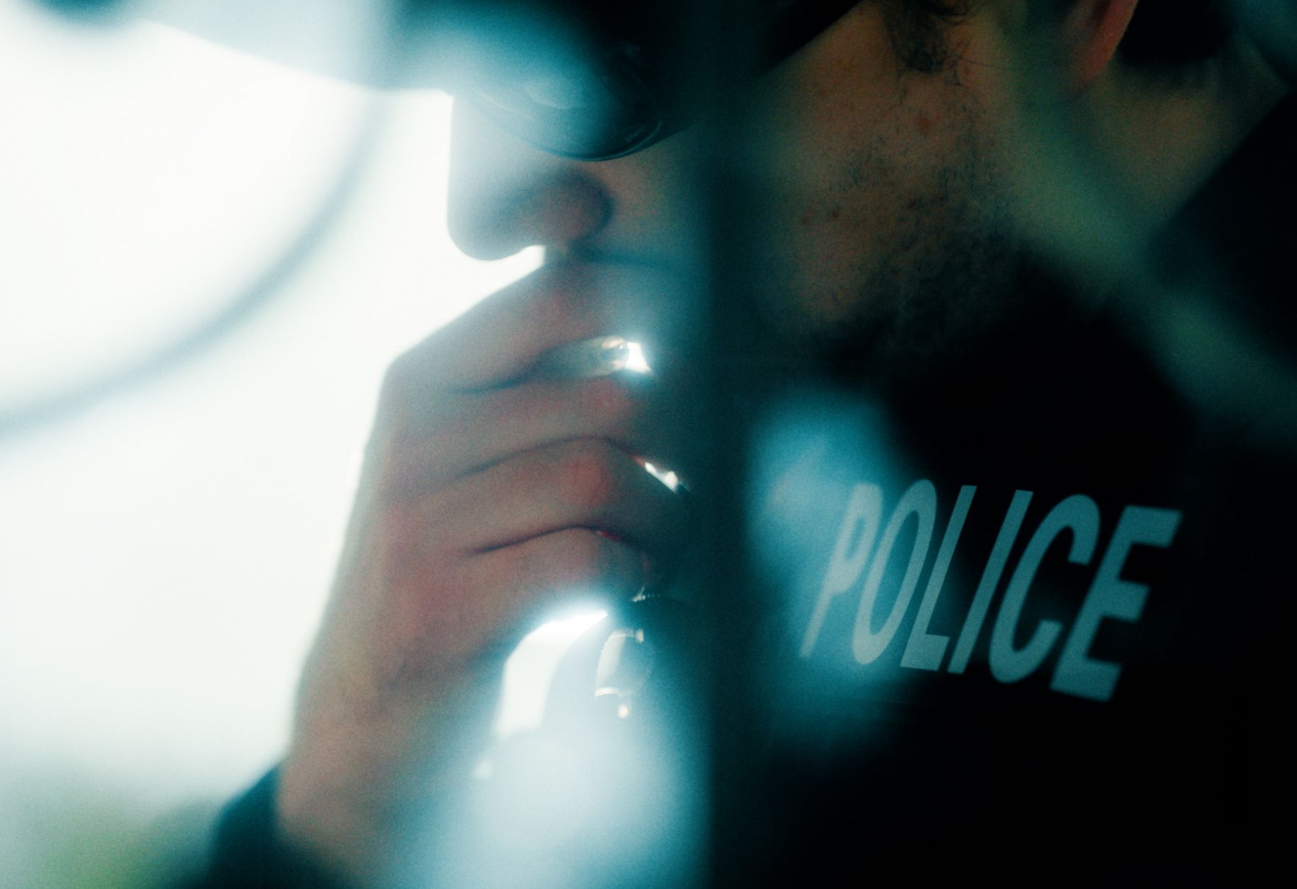 Close-up of a person in a police uniform speaking into a radio, partially obscured by blurred foreground.