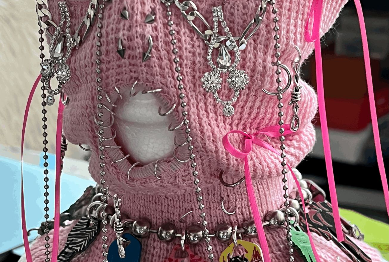 Close-up of a pink knit garment adorned with various silver chains, charms, and neon pink ribbons.