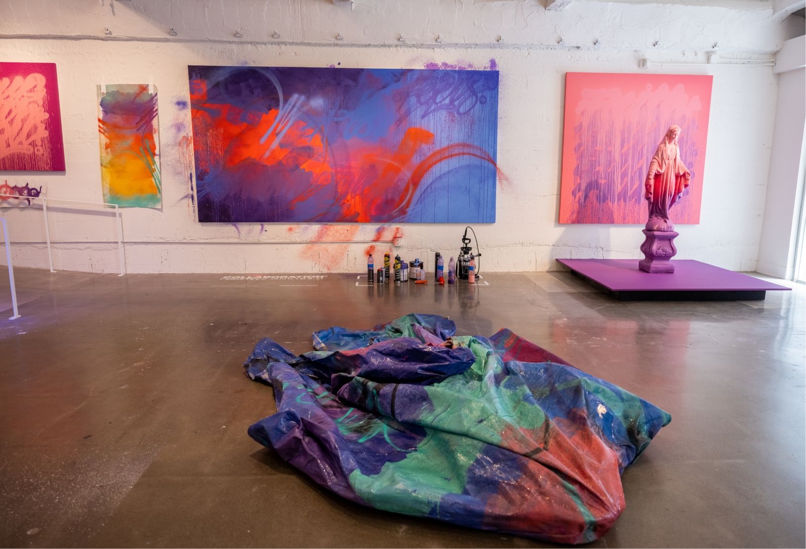 painted tarp sculpture in middle of gallery floor, 4 paintings line the wall and a painted statue of virgin Mary