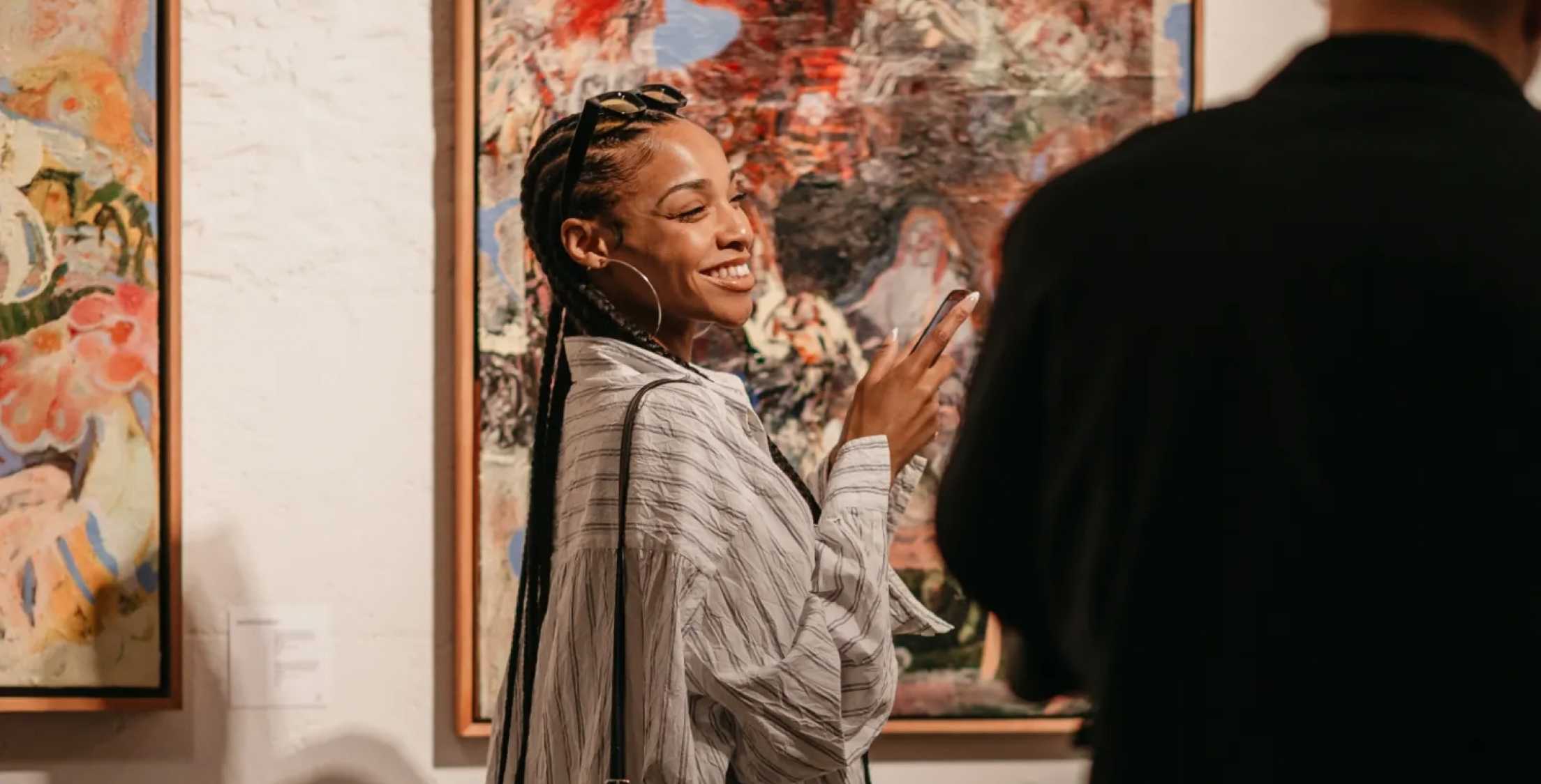 A woman smiles and gestures with her hand while viewing art in a gallery.