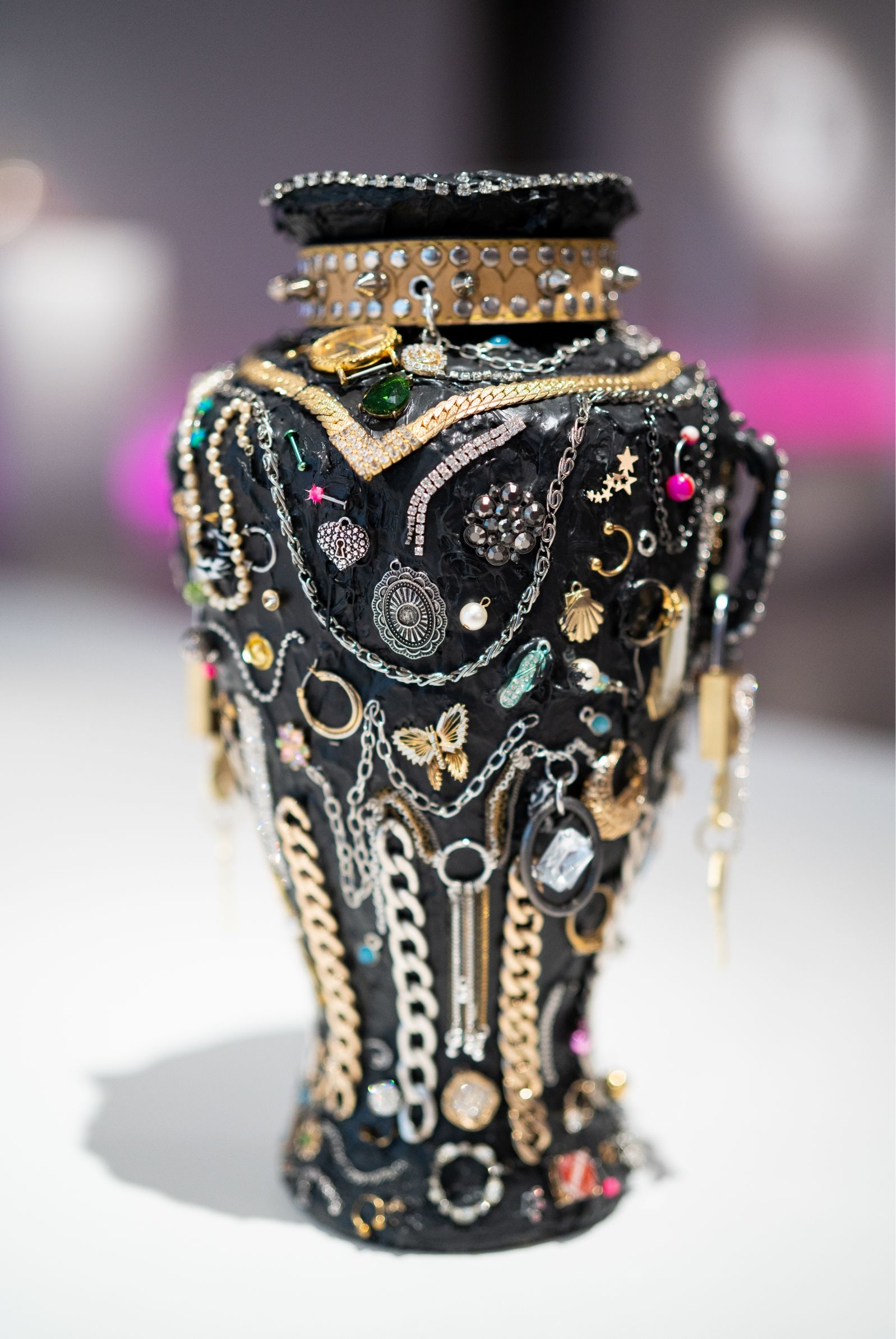 A black vase decorated with various colorful jewels, chains, and metallic embellishments.