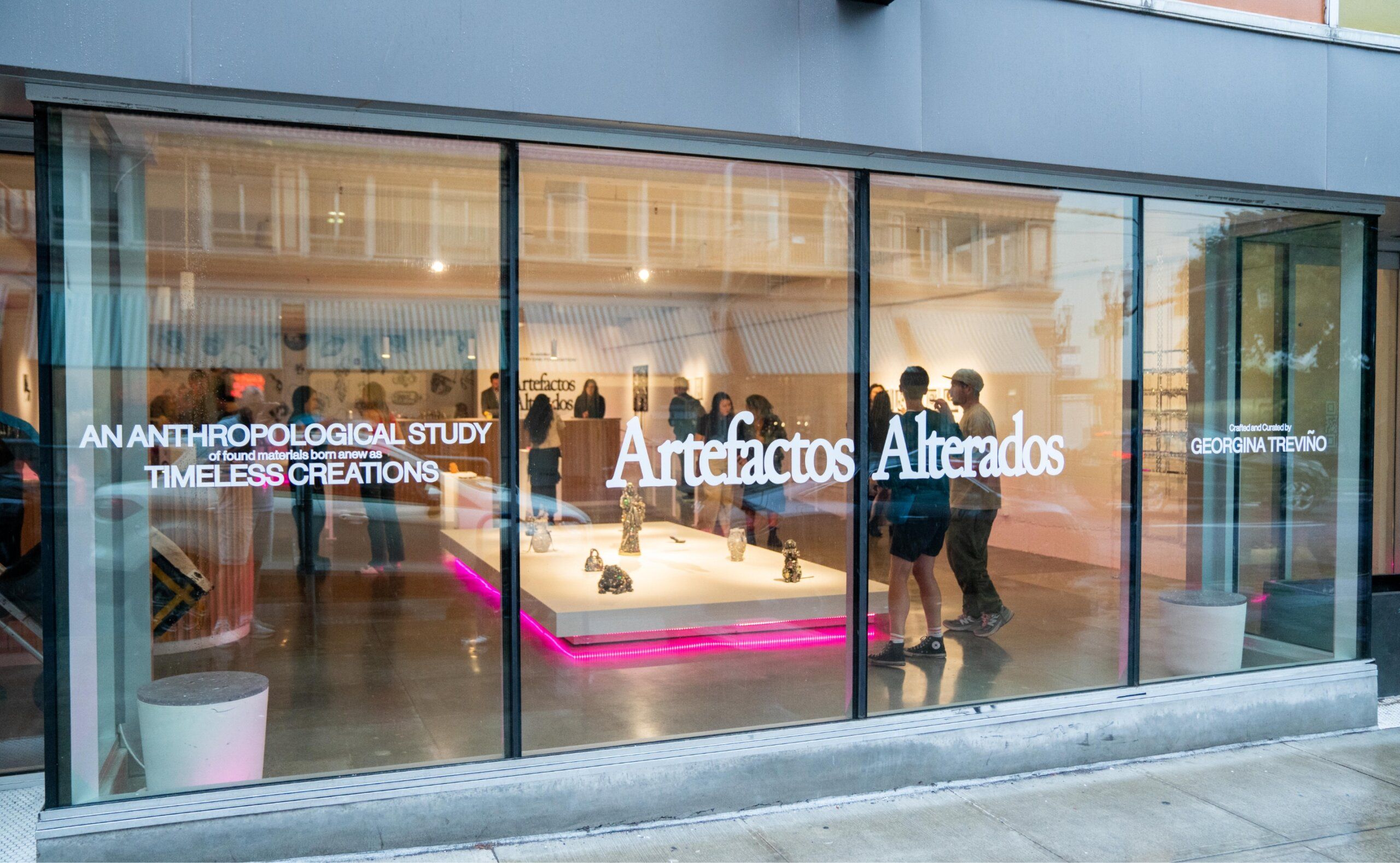 People inside an art gallery with the display "Artefactos Alterados" visible through large street-facing windows.