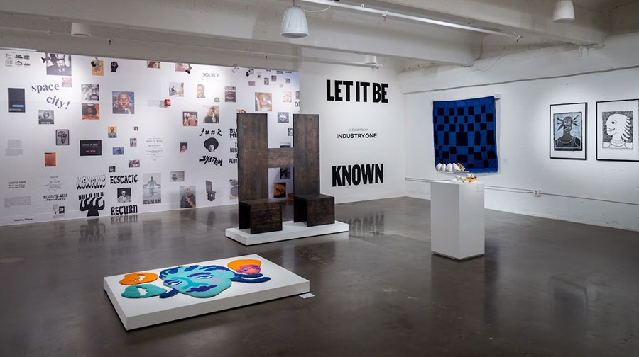 Art gallery with many prints on wall, sculptures on floor, text says Let it be known on the wall