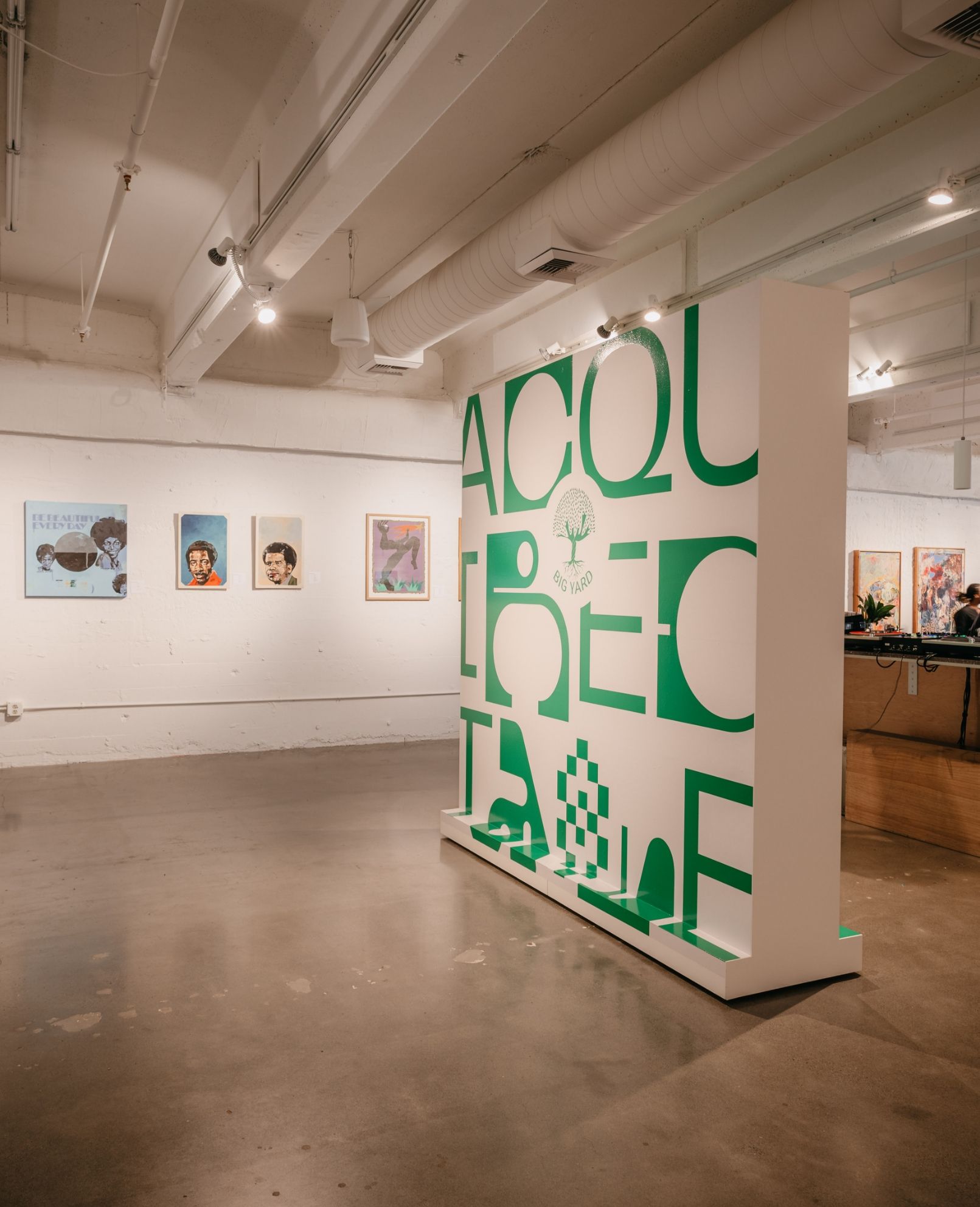 An art gallery with various framed artworks on the walls and a large white installation with green text in the foreground.