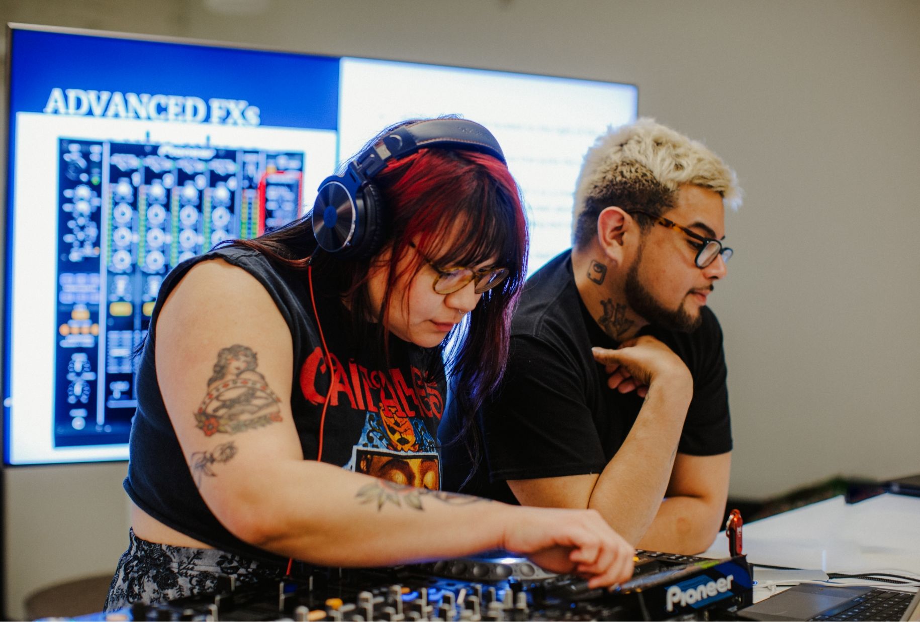 Two people stand behind a DJ mixer