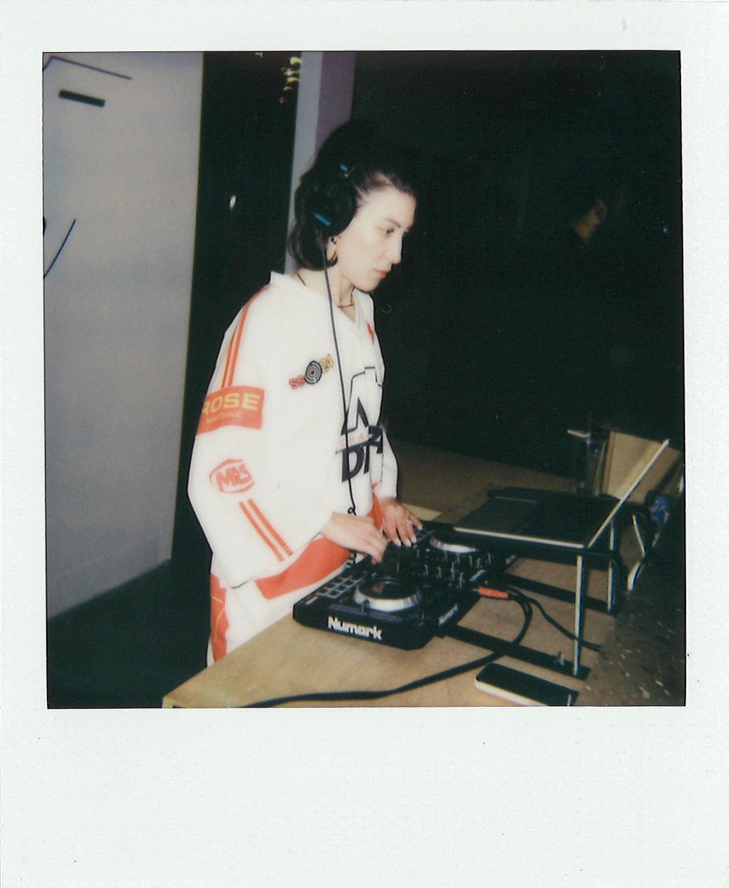 Person wearing headphones and a white jacket operates DJ equipment on a table.