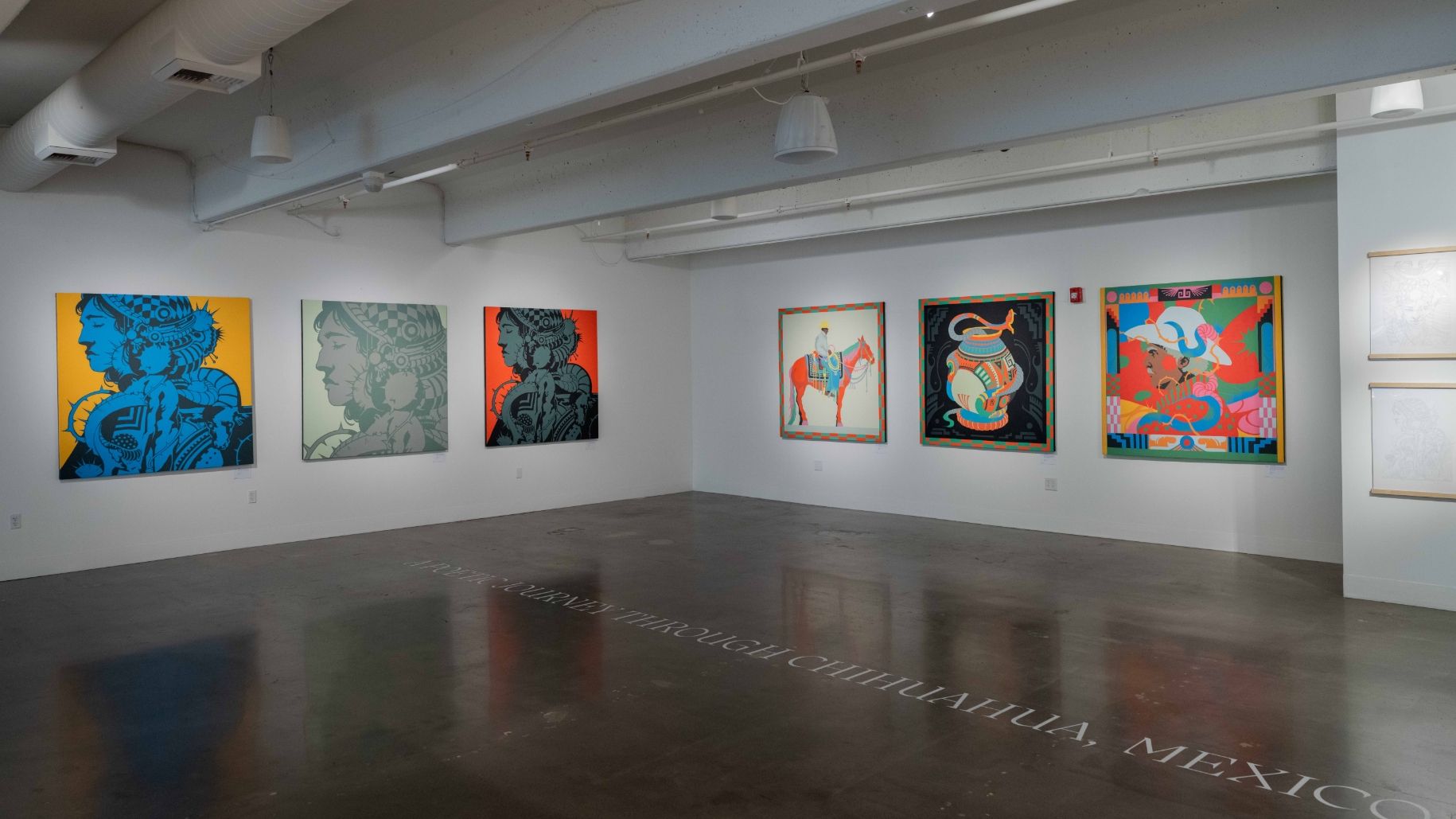 An art gallery displaying colorful, framed paintings on white walls. The paintings depict various abstract and cultural themes. The floor is reflective, and the room has ceiling-mounted lights and ducts.