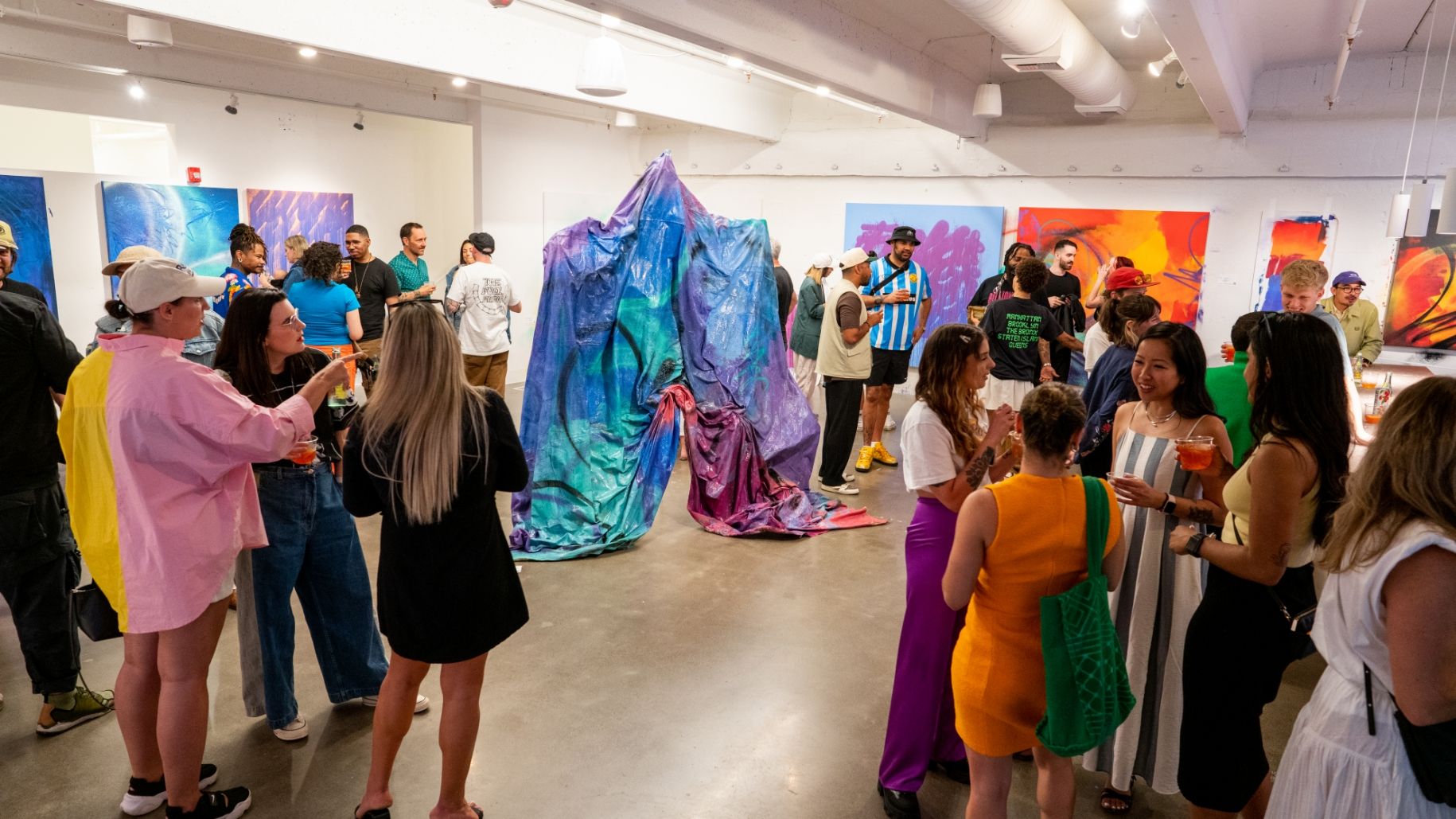 Dozens of people in exhibition opening around painted tarp sculpture