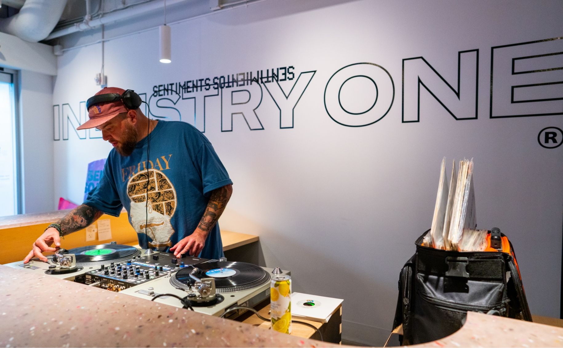 DJ putting needle down on vinyl record. Vinyl stickers on wall behind reads Sentiments Sentimientos Industry One