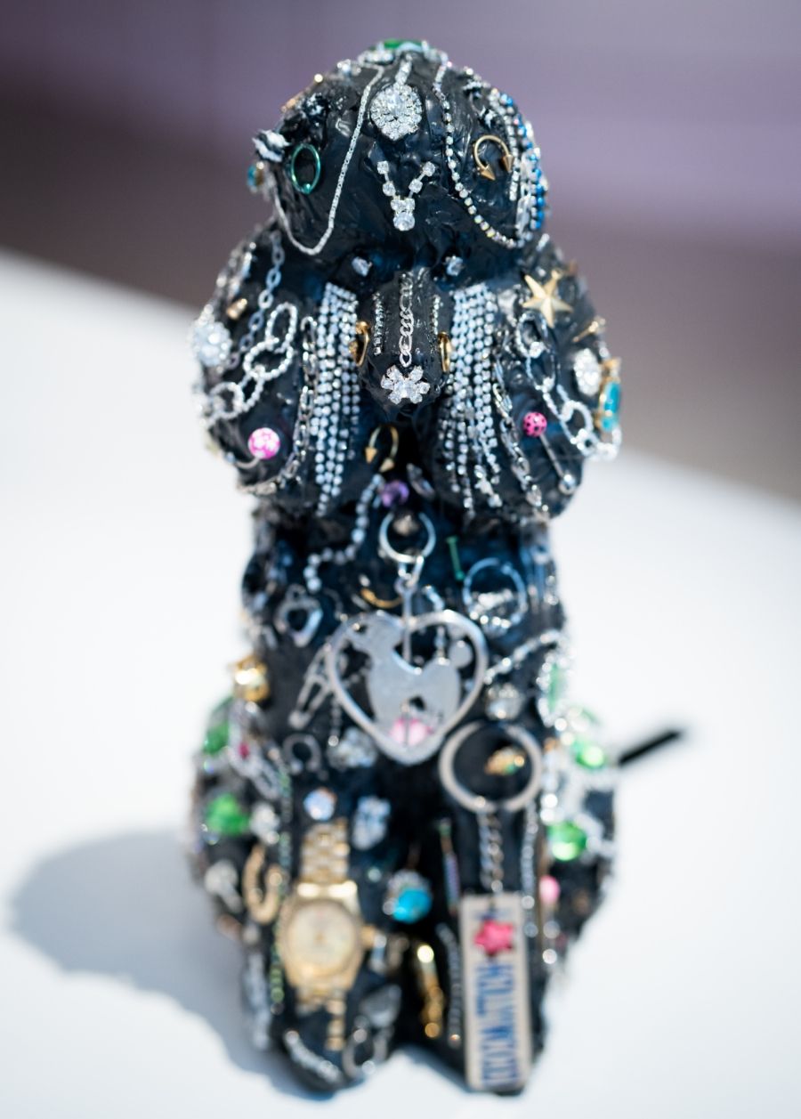 A black dog sculpture adorned with various jewelry pieces, including chains, watches, and decorative items, on a white surface.