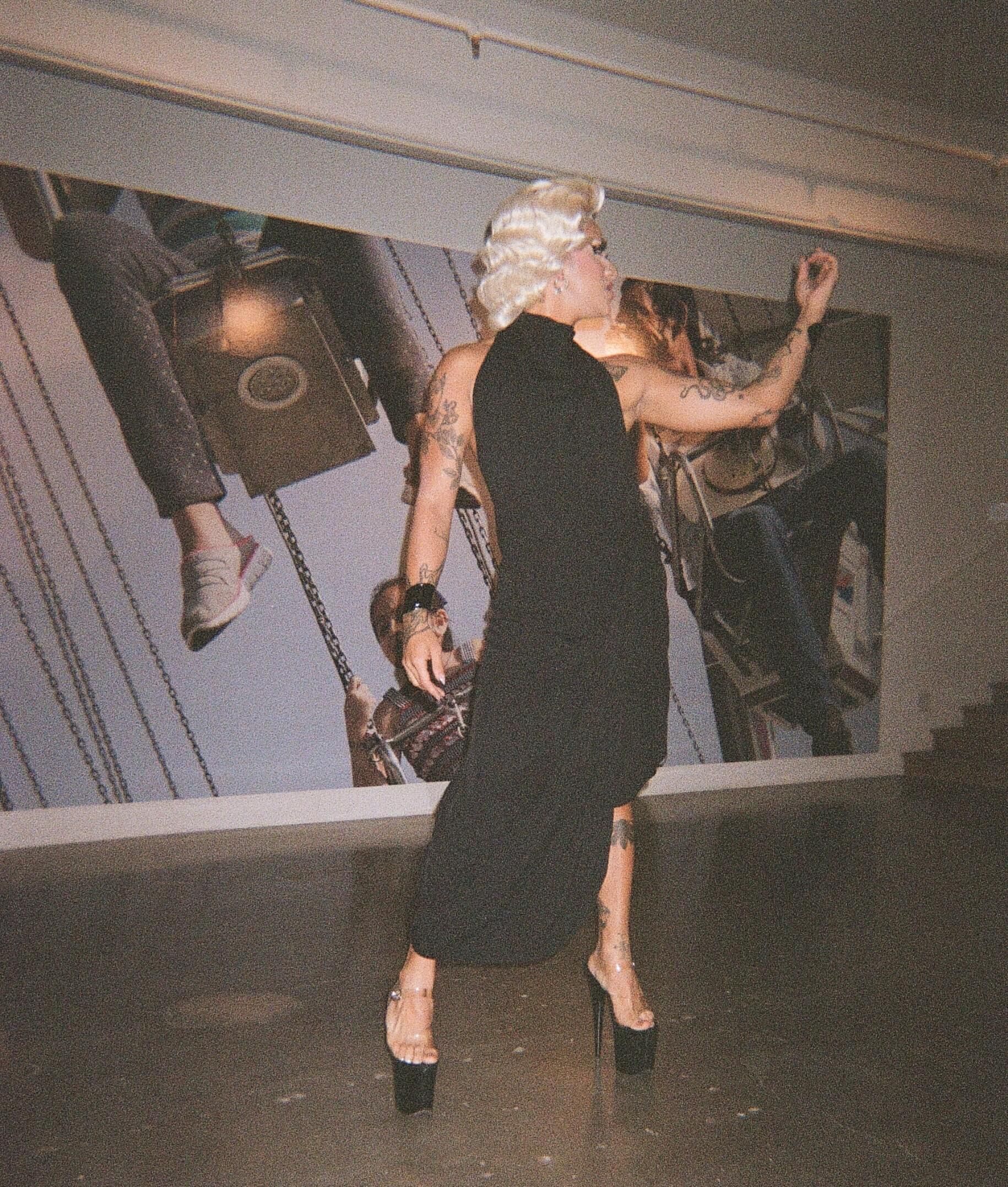 A woman in a black dress performing drag in art gallery.