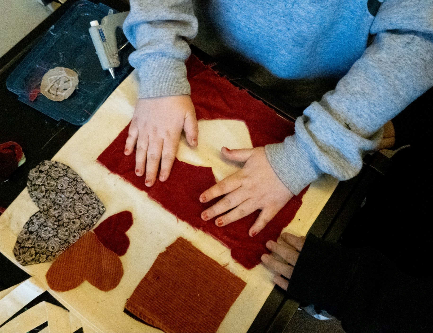 A young person glues down a fabric heart onto a tote bag