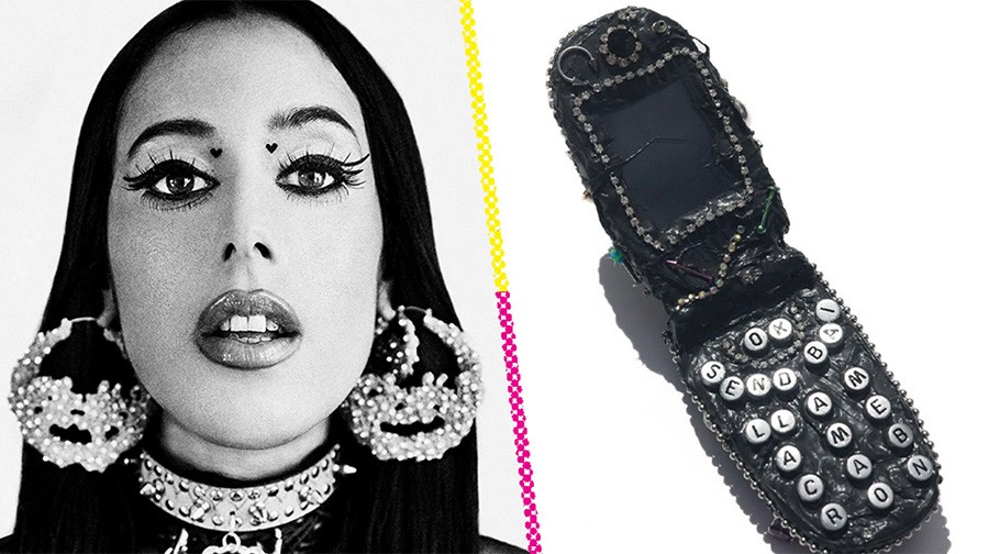 Black and white portrait of a woman with large hoop earrings and facial piercings next to a decorated, bejeweled flip phone with white lettered buttons.