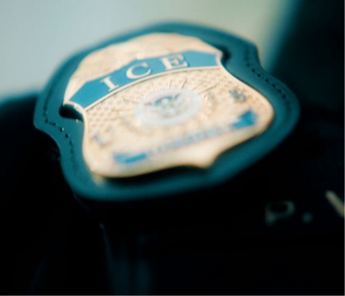 Close-up of a badge with the letters "ICE" on it, attached to a dark surface.