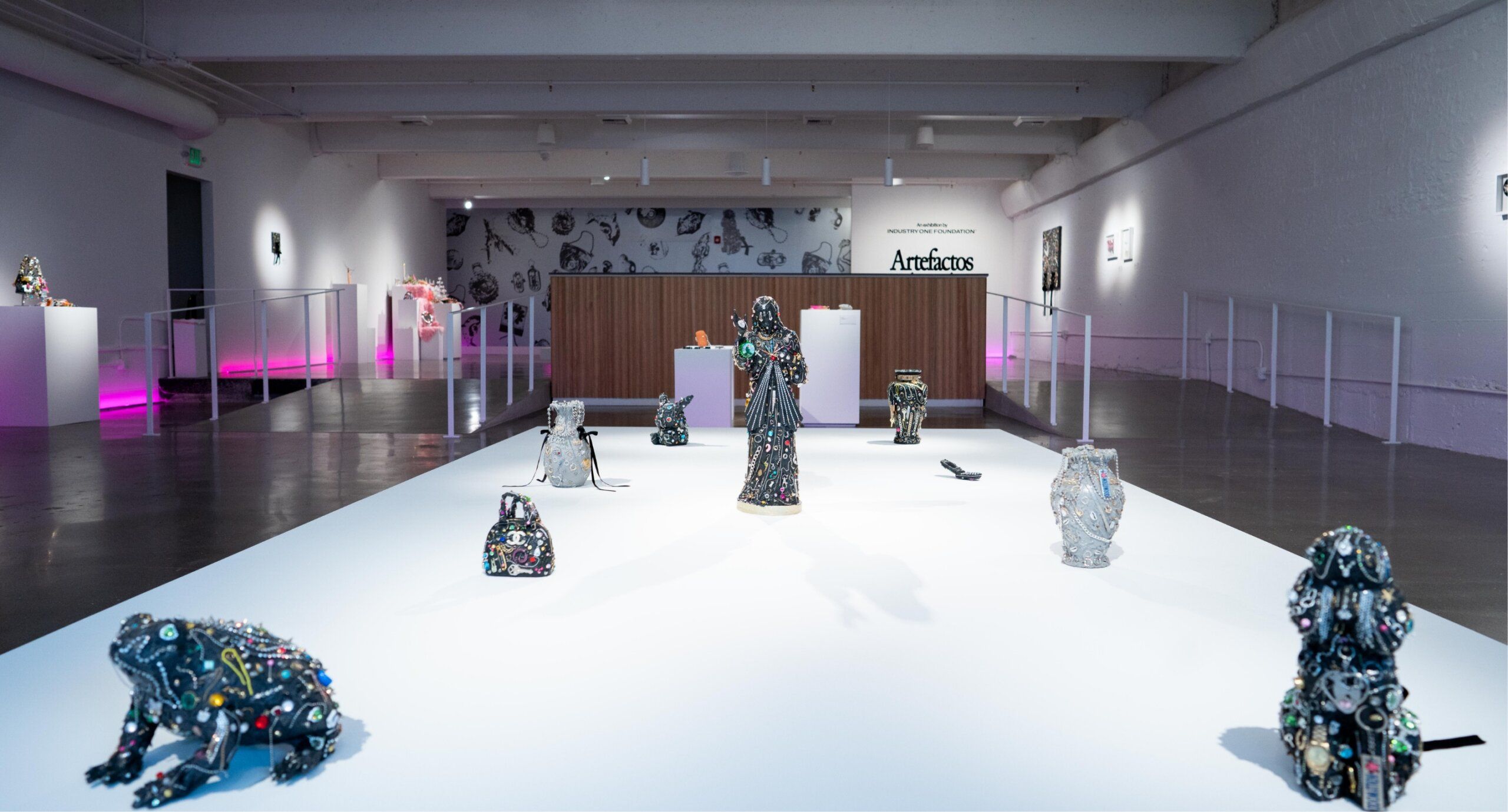 Art gallery featuring various ornate sculptures of animals and figures on a white platform, with a wooden reception desk in the background and pink lighting accents.