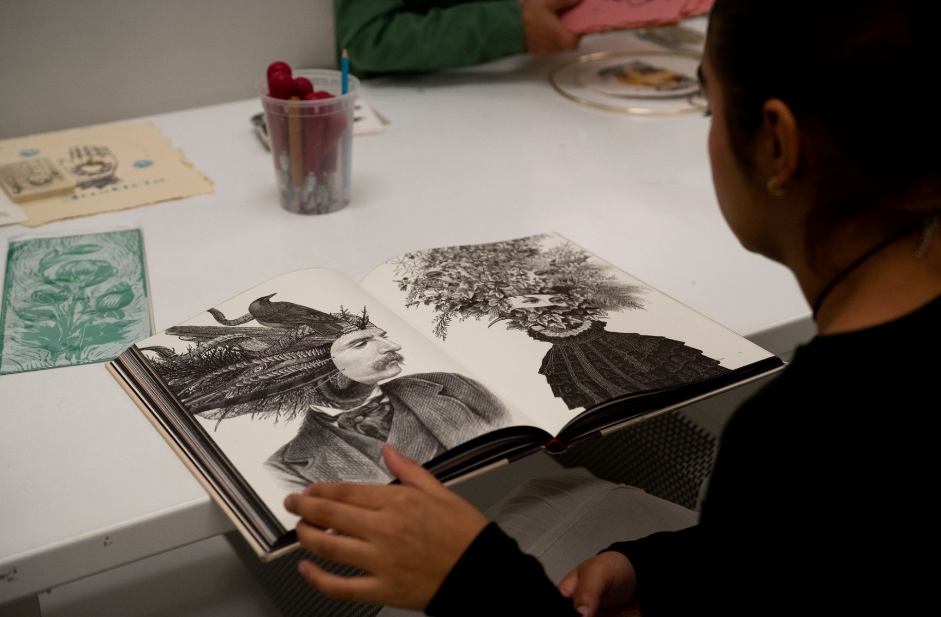A woman is sitting at a table with a book of drawings.