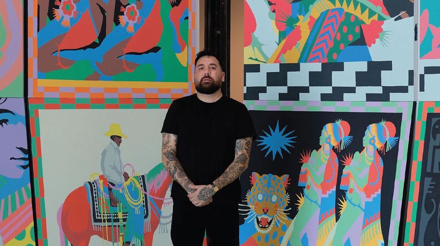 A person with tattoos on their arms stands in front of a colorful mural featuring various patterns, a horse rider, tigers, and abstract shapes.