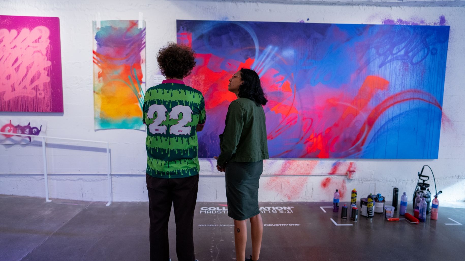 2 people stand in front of large brightly colored abstract painting