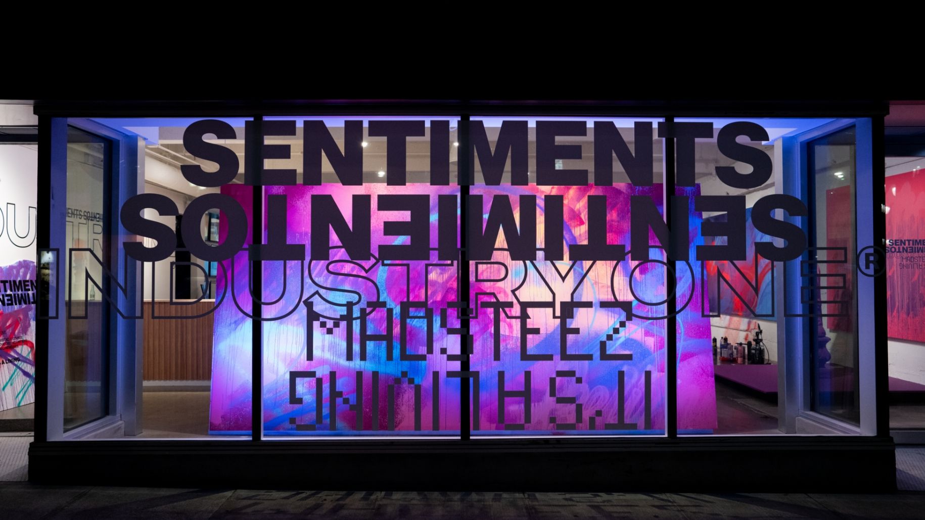 Outside Gallery Storefront window with vinyl stickers reading Sentiments Sentimeientos Industry One Madsteez Its a living