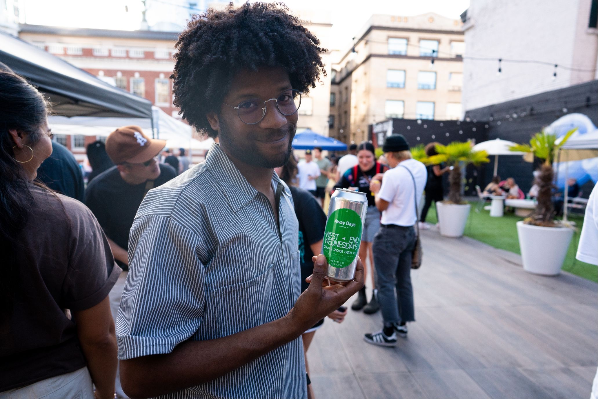 A man with afro hair holding a can of beer with West End Wednesday label.