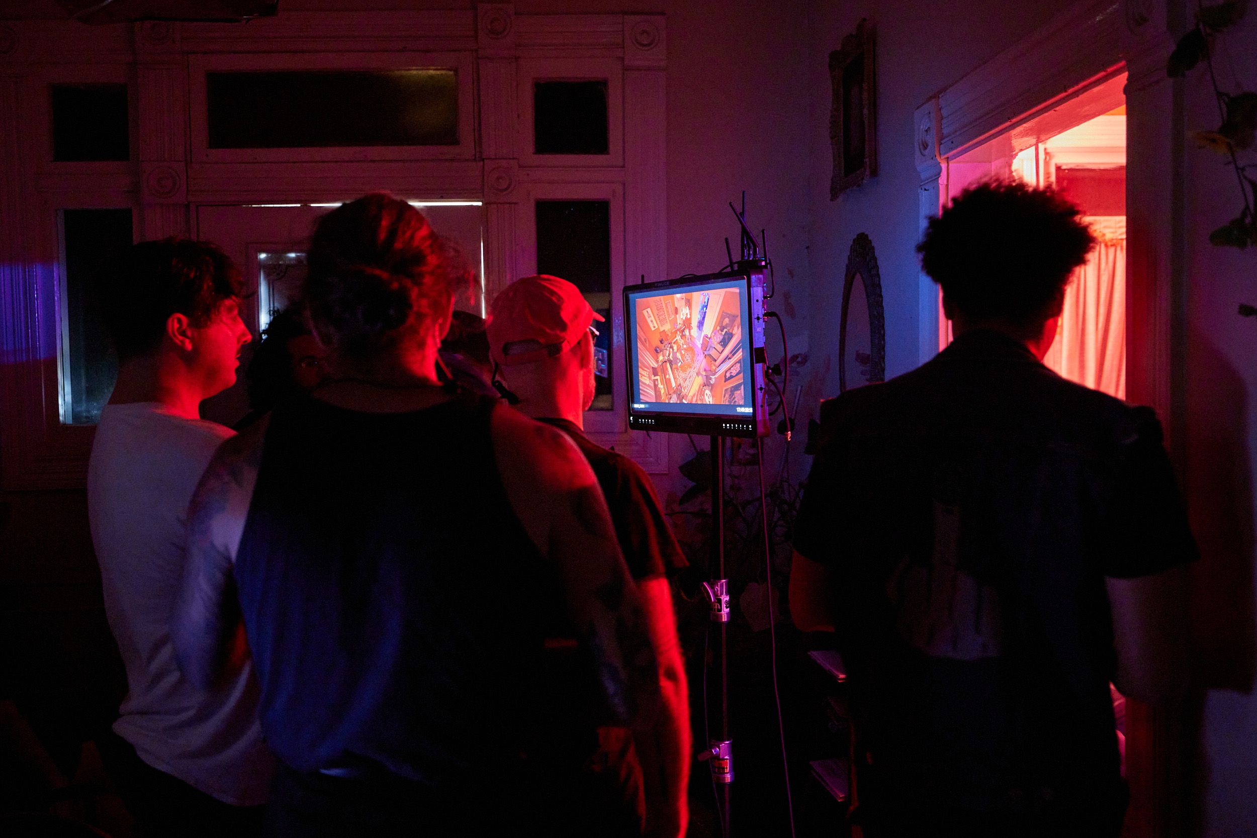 A group of people stands in a dimly lit room, watching a brightly illuminated screen displaying an image.