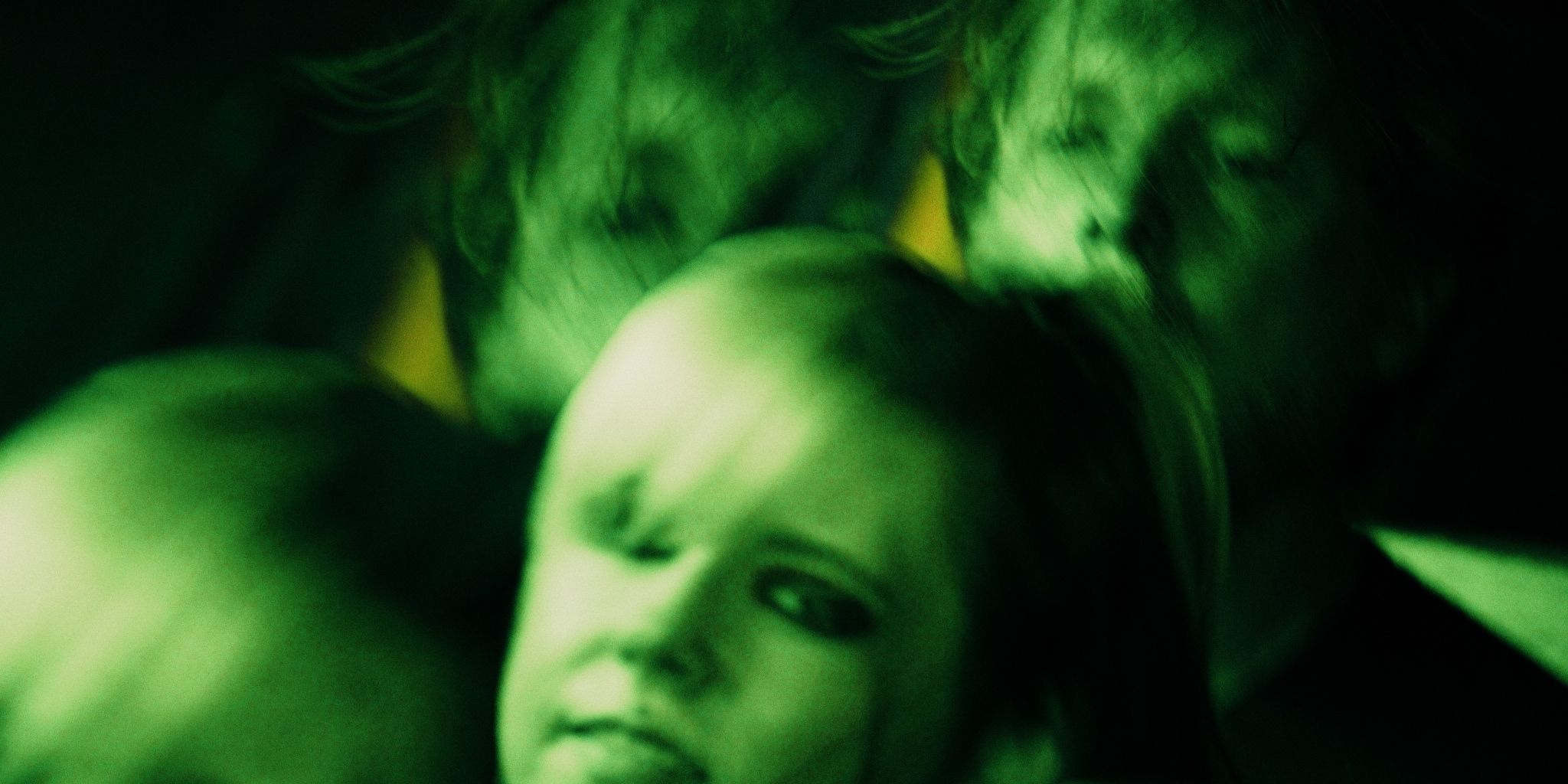 Blurry, green-tinted image of faces with an eerie, distorted appearance.