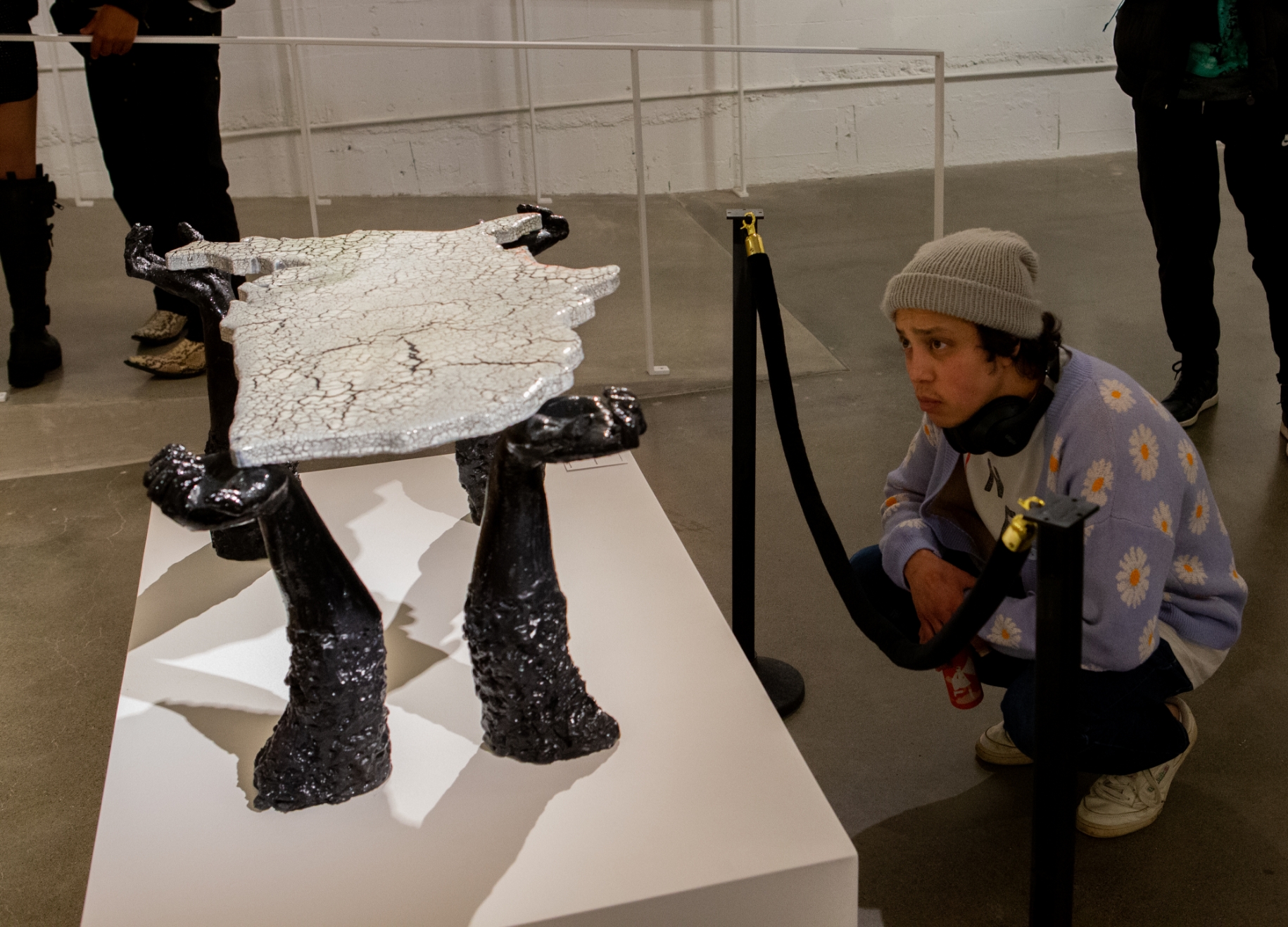 peerson squats down to admire sculpture of 4 black colored hands and arms holding up a map of the United States