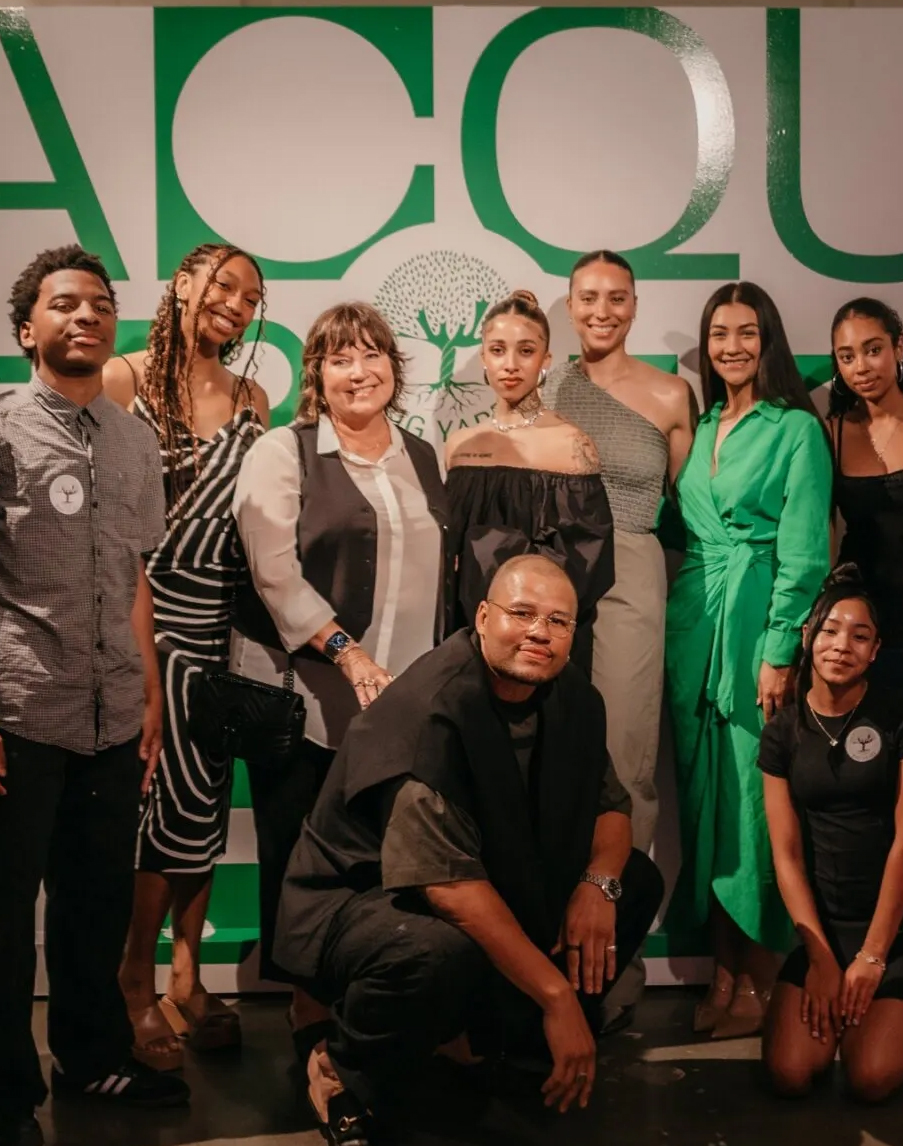 A group of ten people, some standing and some kneeling, posing for a photo indoors in front of a green and white backdrop.