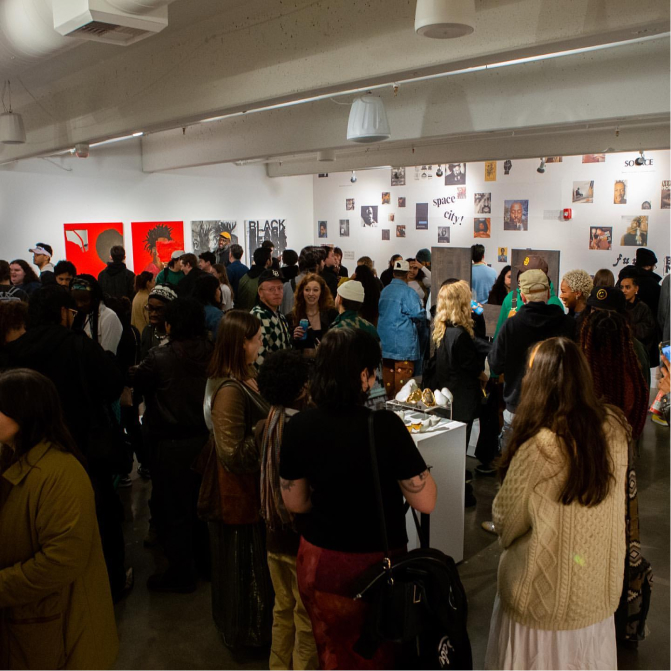 A large group of people attending an art gallery event. Various artworks are displayed on the walls, and attendees are conversing and admiring the pieces.